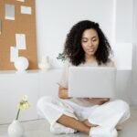 Young woman with curly hair working on her laptop in a cozy home setting, exuding confidence and focus.